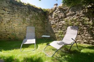 two chairs sitting in the grass next to a stone wall at La Petite Maison du Périgord in Tourtoirac