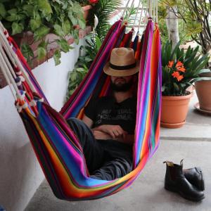 Yellow House Hostel B&B في أنتيغوا غواتيمالا: رجل يجلس على أرجوحة مع قبعة