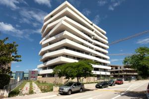 a tall white building with cars parked in a parking lot at Apartman Elena in Split
