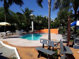 a pool with two benches and a table and chairs at Pousada Recanto Solar dos Pássaros in Olímpia