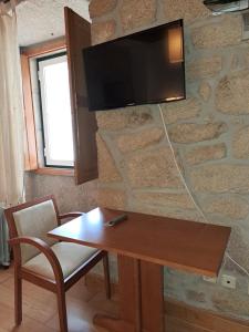 Habitación con mesa y TV en una pared de piedra. en Casa d Toninha - Casas de Campo - Turismo Espaço Rural - AL en Sernancelhe