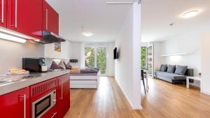 a kitchen with red cabinets and a living room at Anstatthotel Goldau - self-check-in in Goldau