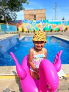 Una niña con sombrero sentada en una balsa rosa junto a una piscina. en Гостевой дом Асель en Cholpon-Ata