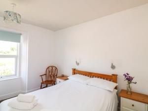 een witte slaapkamer met een bed en een stoel bij Thornlea View in Hope-Cove
