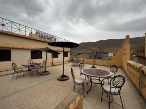 eine Terrasse mit Tischen, Stühlen und einem Sonnenschirm in der Unterkunft Hotel Izlane in Imilchil