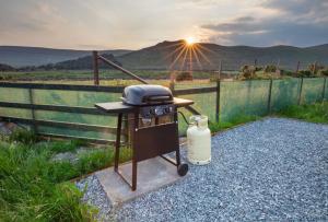 a bbq grill with the sun setting behind a fence at OAKWOOD GLAMPING Mourne Mountains in Moyad