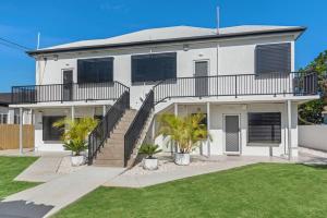 a white house with stairs and palm trees at Sunrise Two Bedroom Apartment in Redcliffe