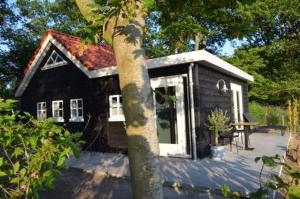 une petite maison noire et blanche avec un arbre dans l'établissement PRIVÉ IN EEN BOSRIJKE OMGEVING Welkom bij gastenverblijf het ontsnapte schaap in Jubbega, à Jubbega-Schurega