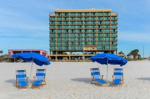four chairs and umbrellas on a beach with a hotel at Phoenix All Suites Hotel in Gulf Shores