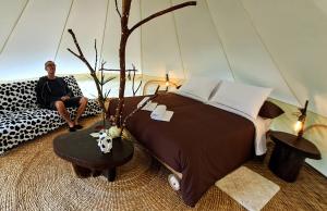 a man sitting on a couch next to a large bed at Finca de la Vaca - Glamping & Camping in Mera