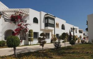 un gran edificio blanco con árboles y plantas delante de él en Charmant Studio vue mer @Kantaoui - 1min à pied de la plage en Hammam Sousse