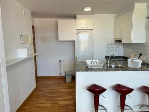 una cocina con armarios blancos y taburetes rojos en Playa Miño, en Miño