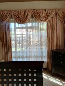 een slaapkamer met een groot raam met gordijnen bij Tjibelu's Nest Guest Home in Lobatse