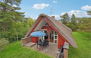 ein rotes Cottage mit einem Strohdach, einem Tisch und einem blauen Regenschirm in der Unterkunft Beautiful Home In Rm With 3 Bedrooms And Wifi in Rømø Kirkeby