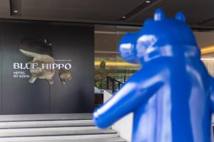 un manichino blu di giocattoli che sta davanti a una finestra di Blue Hippo Hotel a Ban Khlong Samrong