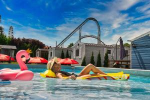 a woman laying on a raft in a swimming pool with a roller coaster at Holiday Park Zator in Zator