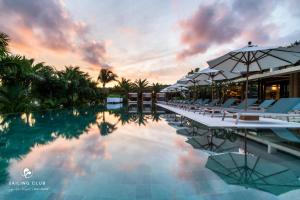 a pool with chairs and umbrellas at sunset at Sailing Club Signature Resort Phu Quoc in Phú Quốc