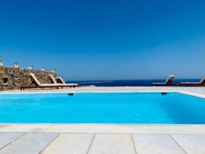 a blue swimming pool with chairs and the ocean at Artemis Sky Villa in Antiparos