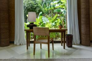 a table with a lamp and a chair in front of a window at NIHI Sumba in Watukarere