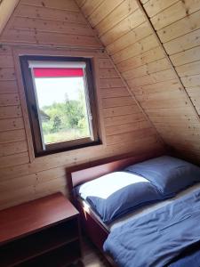 a twin bed in a wooden cabin with a window at Domki Letniskowe - Leśne Zacisze in Jarosławiec