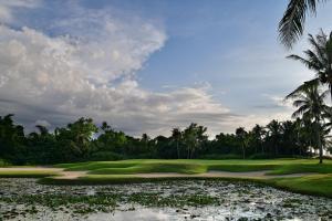 a golf course with palm trees and a pond at The Empire Brunei in Bandar Seri Begawan