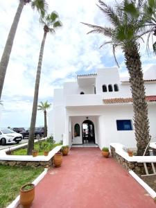 a white house with palm trees and a red driveway at Villa avec jardin sur la plage - Complexe Al Amine in Fnidek