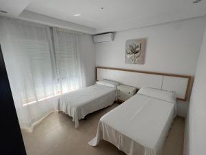 2 camas en una habitación con paredes y ventanas blancas en Apartamentos Flamingo Hills, en Benitachell