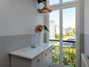 eine weiße Kommode mit einer Vase mit Blumen darauf neben einem Fenster in der Unterkunft Villa Amelia, App. 07 in Heringsdorf