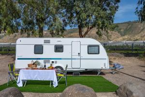 a white caravan parked next to a table with food on it at Dream Caravan's - קרוואנים מושלמים למשפחות בחוף כורסי בכינרת in En Gev