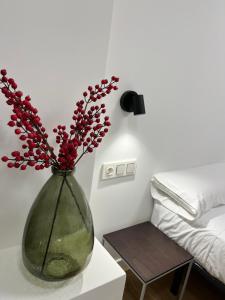 a vase with red flowers on a table next to a bed at Anzaran in Irún +3 photos