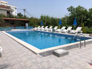 una piscina con sedie bianche e ombrelloni blu di Guest House Green Garden a Ulcinj