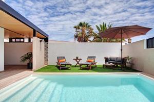 een zwembad met 2 stoelen en een tafel en een parasol bij Villa Toro in Corralejo