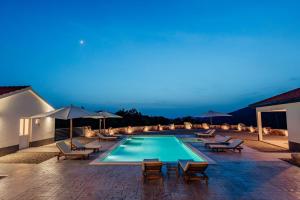 a pool with chairs and umbrellas at night at Vila Agape with a pool, football and tennis court in Lovreć
