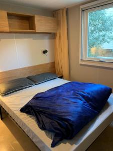a bed with a blue blanket on it in front of a window at Mobil Home La Palmyre Camping Bonne Anse 4 étoiles in Les Mathes
