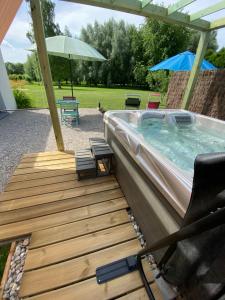 a hot tub on a wooden deck with an umbrella at gite du vieux saule et spa in Vieil-Hesdin