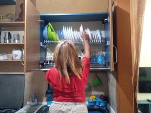 a woman is reaching for dishes in a cupboard at Pozzuoli 100per100 Home in Pozzuoli