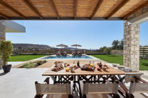 un tavolo e sedie in legno su un patio con piscina di Alba Lilia Cretan Villas a Pitsidia