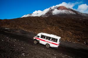 a white bus driving down a dirt road with a mountain at Case Gemmellaro - Family&Friends in Nicolosi