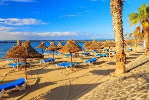 einen Strand mit Strohschirmen und -stühlen und dem Meer in der Unterkunft Modern apartment in Las Americas, LK520 with pool close to the ocean in Playa de las Americas