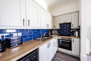 una cocina con armarios blancos y azulejos azules en Flat 3 Flint House Tenby - Luxury couples apartment, en Tenby