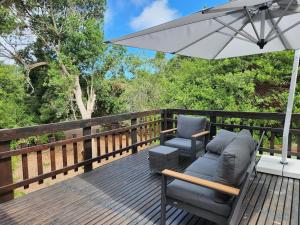 eine Terrasse mit 2 Stühlen und einem Sonnenschirm in der Unterkunft Nature's Edge Cabin in Natureʼs Valley