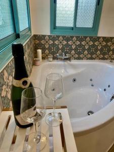a bottle of wine and two glasses on a table next to a bath tub at heart of the golan heights cabin -בקתה במטע in Eli Ad