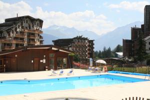 a swimming pool with chairs and mountains in the background at Résidence Saboia Clés Blanches in La Tania