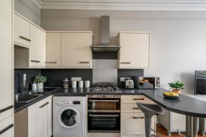 eine Küche mit weißen Schränken, einer Waschmaschine und einem Trockner in der Unterkunft The Holyrood Park Apartment in Edinburgh