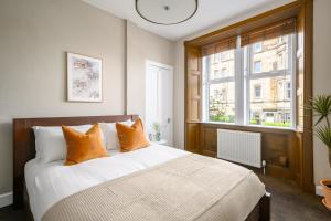 ein Schlafzimmer mit einem Bett mit orangefarbenen Kissen und einem Fenster in der Unterkunft The Holyrood Park Apartment in Edinburgh