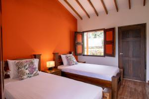 Duas camas num quarto com uma parede laranja em HOTEL YANUBA CAMPESTRE em Pereira
