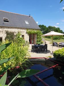 a house with a table and chairs and an umbrella at Le Domaine de la petite chèvre in Ploumagoar