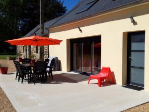 un patio con mesa, sillas y sombrilla roja en Gîte Avec Spa et Sauna Privatifs, en Poullaouen