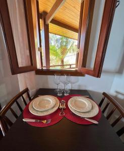 a table with two plates and glasses and a window at Pousada Nascer da Lua in Monte Verde