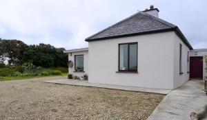 a white house with a garage and a driveway at Meadow Cottage in Belmullet